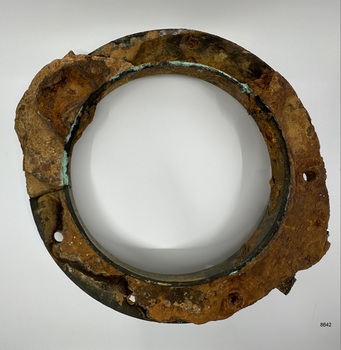 Encrusted and verdigris surface of round porthole. Parts of fittings still attached.