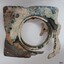 Square metal frame with a band round a central opening. The frame has formed holes. A handle is visible.