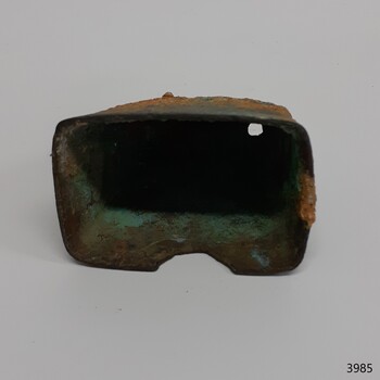 Rectangular base with small half circle cut from one long edge, handle hole in top end, corroded