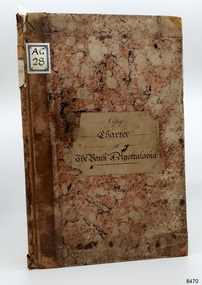 Large book, front cover and spine. Cover is pattern of brown, cream and black pebble shapes. Handwritten label is in centre