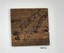 Small square of dark brown wood with handwritten inscription.