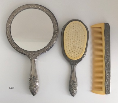 Front view of a three-piece vanity set that includes a hand mirror, hair brush and comb. 