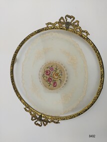 Round tray with a gilt brass border, filigree handles and embroidered doily encased in glass.