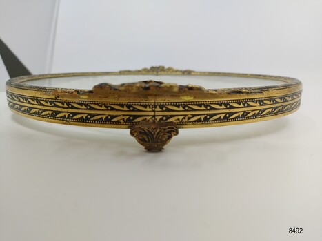 Close up view of brass tray border and foot showing decorative gilt detail.
