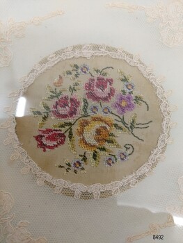 Circular Petit Point embroidery of a bouquet of five large pink, yellow and mauve flowers plus some smaller buds bordered with net and lace.