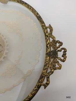 A closeup view of the filigree handle, the top of the gilt border of the tray and the embroidered net.