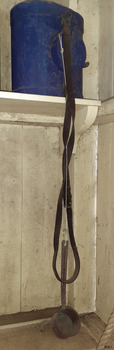 Blue canteen on shelf resting on an oval end, with leather strap hanging along with ladle
