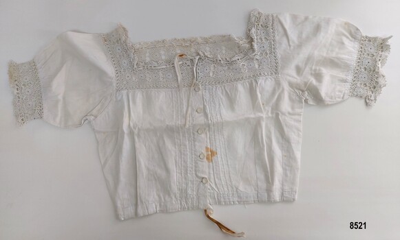Front view of a white, cotton corset cover with pintucks, lace trim, buttons and drawstring at neck and waist
