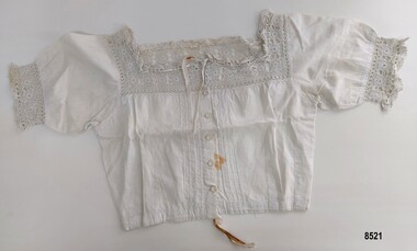 Front view of a white, cotton corset cover with pintucks, lace trim, buttons and drawstring at neck and waist