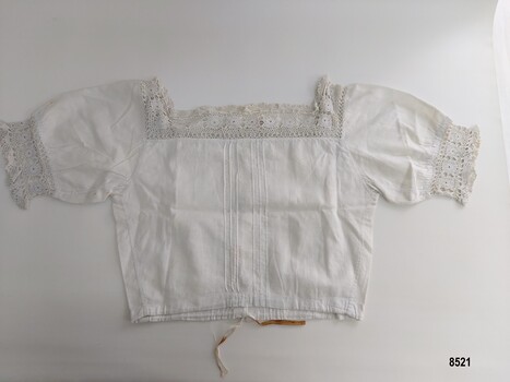 Back view of a white, cotton corset cover with short sleeves and decorated with hand crocheted lace and pintucks.