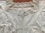 A square neckline with a drawstring cord, decorated with a crocheted lace trim in a floral design, pintucks and feather stitch embroidery.