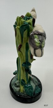Stork standing on a black mound, with tall bullrushes & water-lily pads.