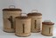 Four cream metal canisters with domed lids with handles attached. Vertical labels on front