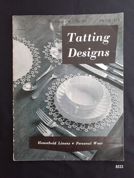 Front of soft covered book has a place setting laid out on a tatted place mat