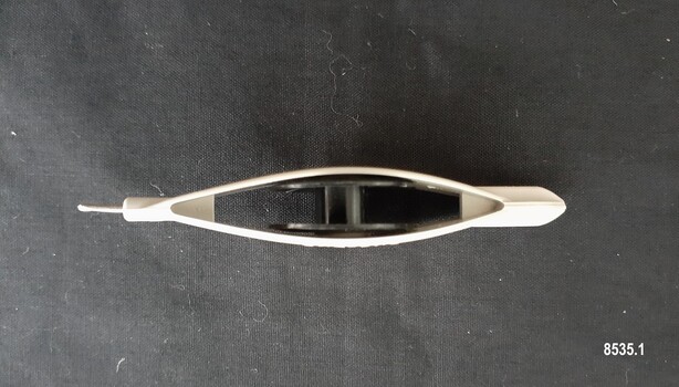 Side view of beige plastic boat shaped tatting shuttle showing the black plastic removeable bobbin inside and the enclosed ends