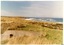 Curved concrete structure in grassy field, in front of tree-bordered fields, building, surf sea 