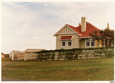 Cream double fronted weatherboard home with red room and three chimneys. Cream picket fence in front.