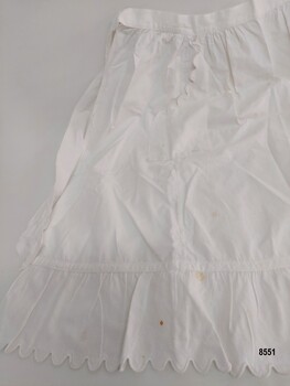 Hem of white cotton apron showing gathered frill with a scalloped edge