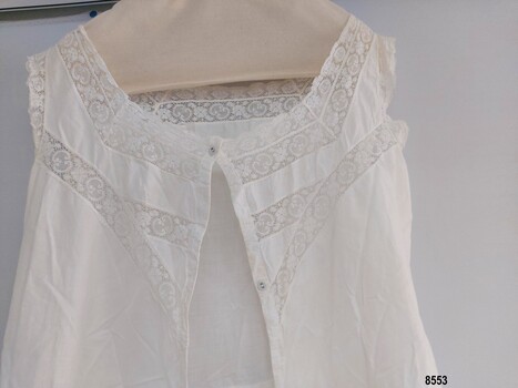 Front of lady's combinations showing lace trim on neckline, arm holes and in a diagonal design on the bodice plus two (of the four) buttons on front opening