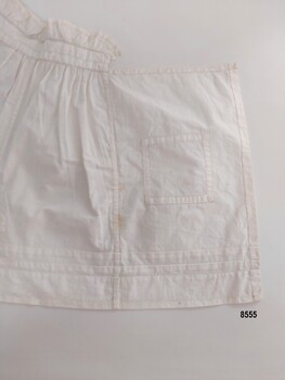 Back of left side of cotton sampler showing hand stitching on patch, seams, hem and frill