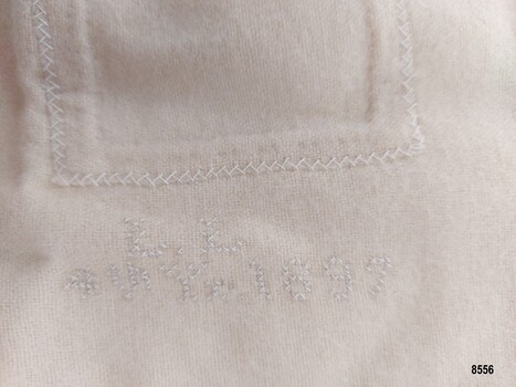 White cross stitch on flannel showing initials L L and date 1897