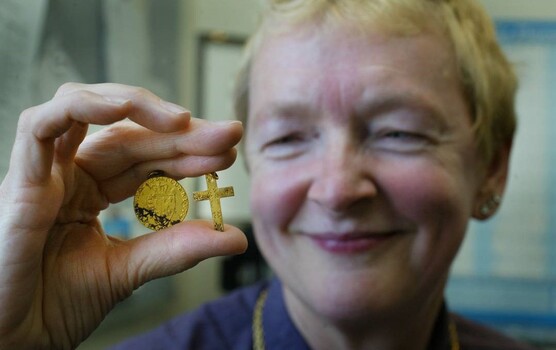 Female smiling and holding a gold coin and gold cross