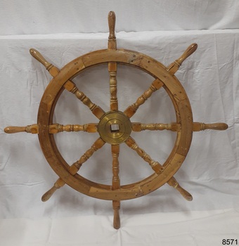 Wooden ship's wheel has turned spokes and brass hub