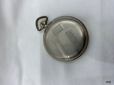 Back view silver coloured fob watch showing lined pattern.