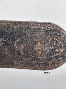 Close up view of an indistinctive maker's stamp on the end of the leather strap