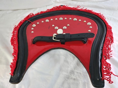 Back of a red and black vinyl covered Housen showing the attaching strap and decorated with a red fringe and silver coloured studs