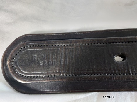 End of wide leather strap with a maker's stamp reading "R. Mitchell Saddler"
