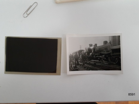 A small black and white photograph of two steam locomotives that appear to have collided head on. There is a carriage behind one of the locomotives and several men are standing around.