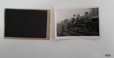 A small black and white photograph of two steam locomotives that appear to have collided head on. There is a carriage behind one of the locomotives and several men are standing around.