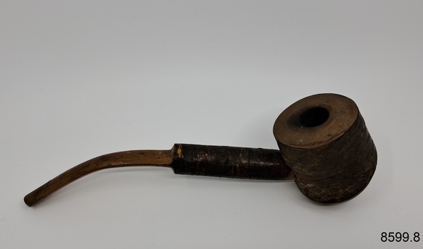 A collection of six pipes. Two of the pipes are resting in their protective cases. One of the pipes is the old fashioned clay type.