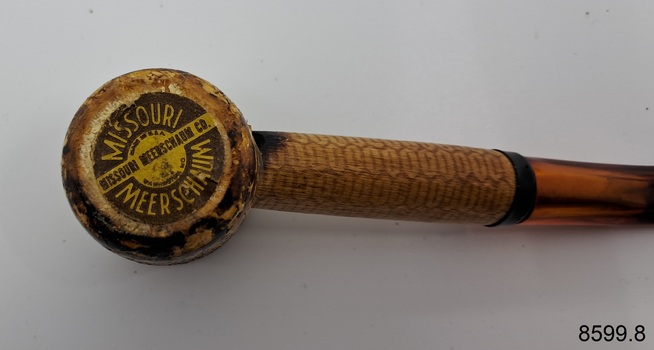 A collection of six pipes. Two of the pipes are resting in their protective cases. One of the pipes is the old fashioned clay type.