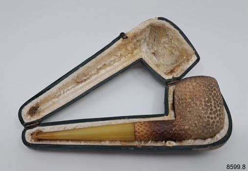 A collection of six pipes. Two of the pipes are resting in their protective cases. One of the pipes is the old fashioned clay type.