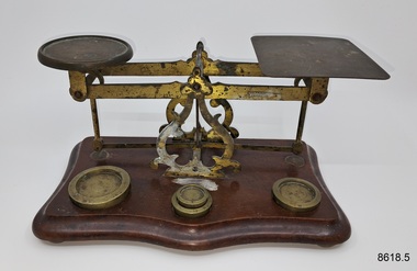 Set of metal scales on wooden base together with four different weights.