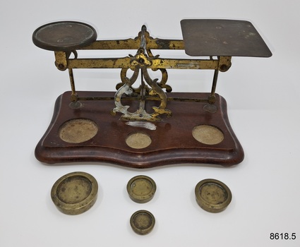 Set of metal scales on wooden base together with four different weights.