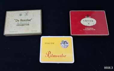 Three metal boxes, once containing cigarettes or cigars branded 'Ritmeester', 'Craven A' and 'De Reszke'.