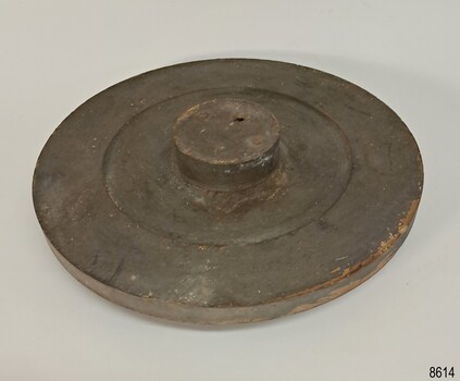 Brown wooden disk with indented centre with a round flat top wooden handle attached the middle