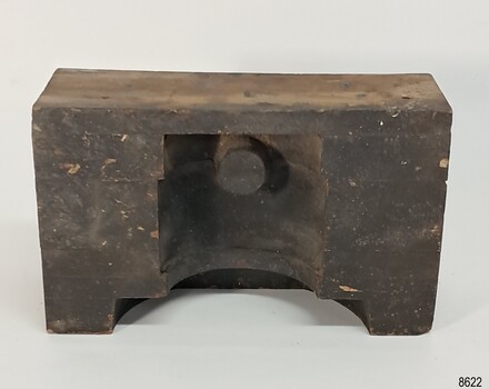 Black block of wood with curved shapes carved out of th and a cylindrical knob shpe left in place