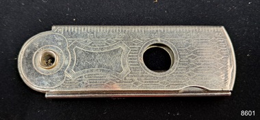 Silver cutter with measurements marked along one side a hole in the centre and the end, and inscriptions