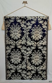 Dar blue and cream richly patterned brocade fumaric hanging from a rod with tastels.