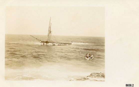Postcard with sepia photo of a sailing ship foundering near a large rock