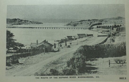 Road alongside a river with buildings on the banks and a bridge from one bank to the other