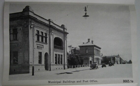 Left side of a street with two storey and one storey buildings and vintage cars