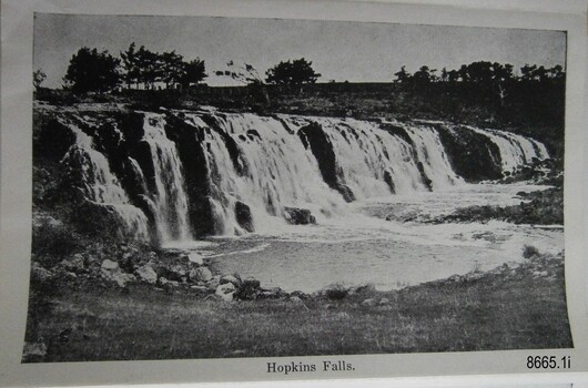 Wide waterfall with river below and treas and building in the background
