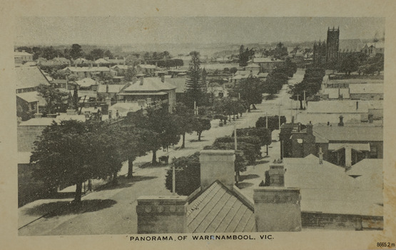 A tree lined street with a turreted building at the end and buildings either side of the street