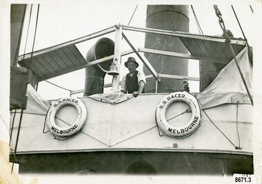 A man is leaning against the rail of a Tugboat. Two lifebuoys are tied to the side of the deck.