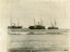 Black and white photograph of three steamers at anchor in a bay. A small rowing boat with crew is on the right.